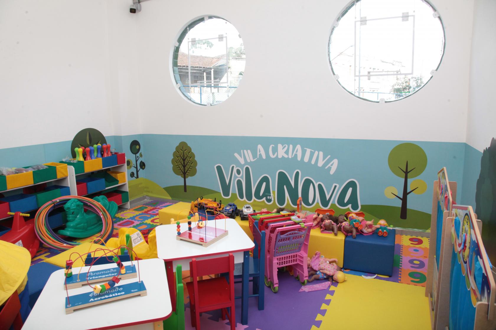 Sala para atendimento de crianças, com mesas e cadeiras em tamanho reduzido, tapete de EVA e pintura na parede. #Pracegover