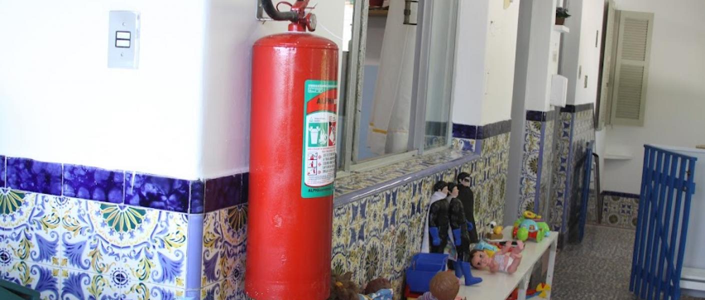 extintor afixado em parede com móvel aberto em baixo e várias caixas com brinquedos. #paratodosverem