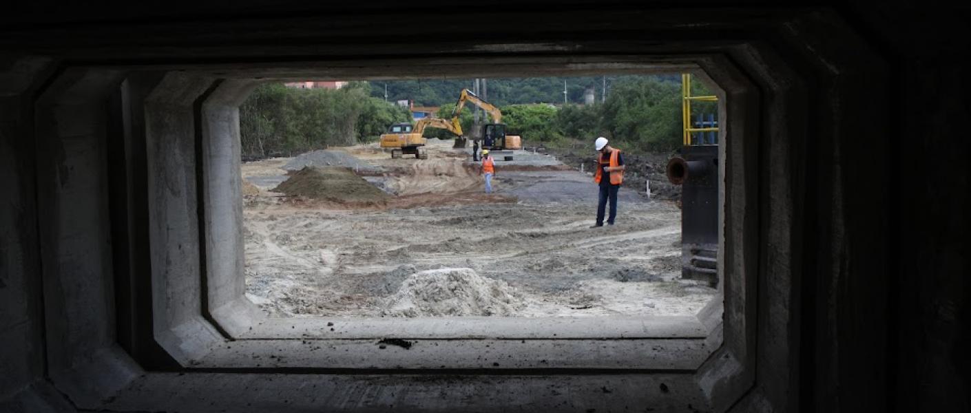 fotógrafo se posicionou na entrada de aduela para fazer dela uma moldura e mostrar a sua proporção em relaão ao homem e máquinas que estão no fundo. #paratodosverem
