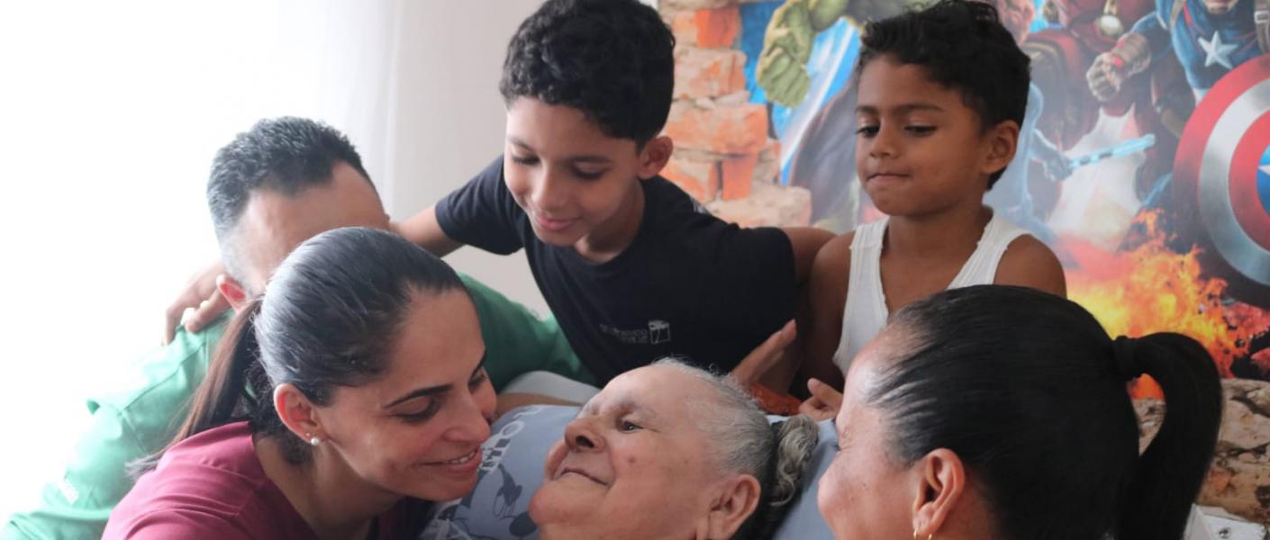 filhos e netos olham com carinho para matriarca sentada #paratodosverem