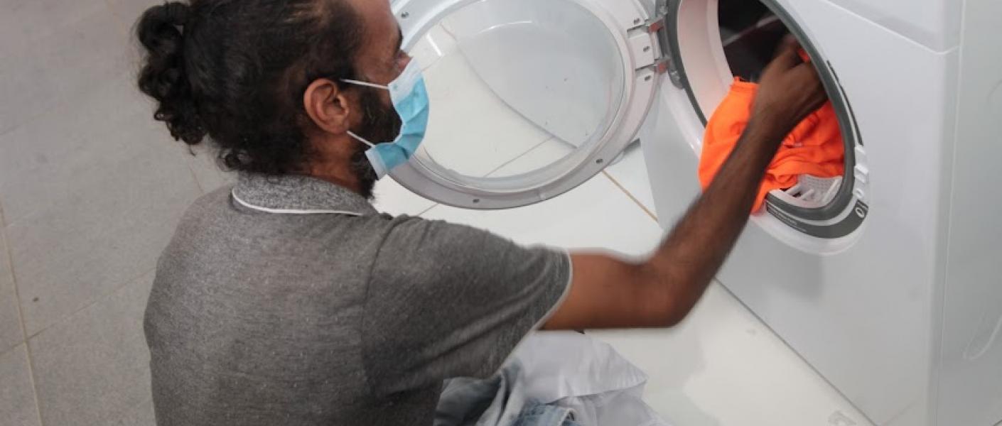 Usuários podem lavar as próprias roupas com toda a estrutura. Homem retira roupas de máquina de lavar. #pratodosverem