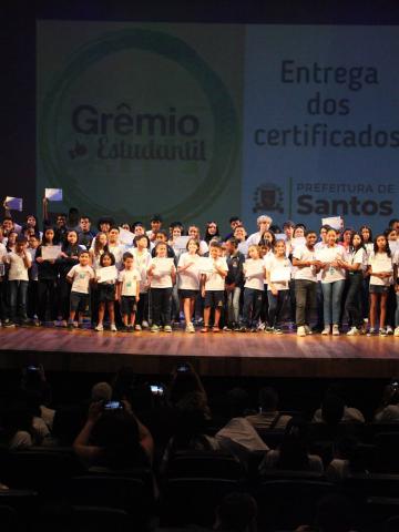 crianças seguram diploma em palco. #paratodosverem