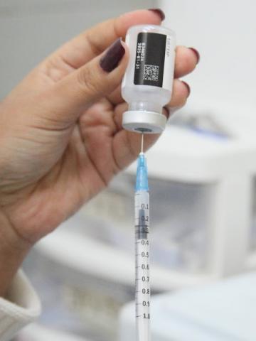 mão segura seringa e frasco de vacina. #paratodosverem 