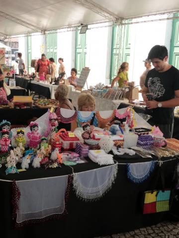balcão com exposiçõ de artesanato e público em torno,. #paratodosverem
