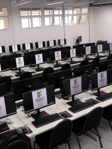 sala de aula com mesas e desktops. #paratodosverem