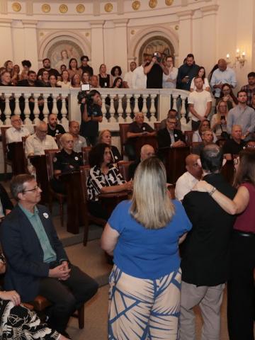 sala lotada com pessoas sentadas e em pé #paratodosverem