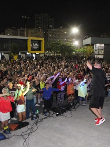 público dança diante de palco animado por instrutor. #paratodosverem