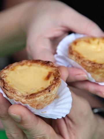 mãos seguram dois pastéis de Belém. #paratodosverem 