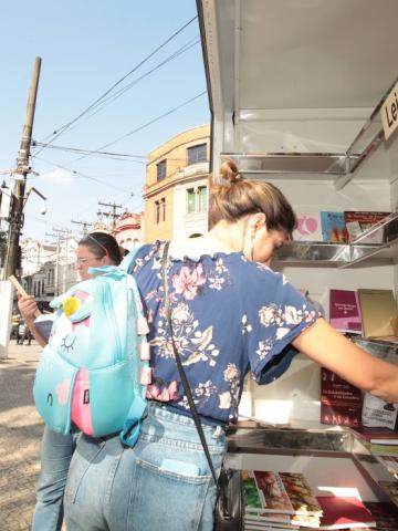 mulher pega livros no estande #paratodosverem 