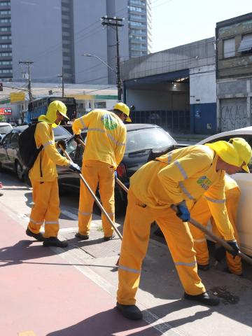 homens varrem guia de calçada. #paratodosverem 