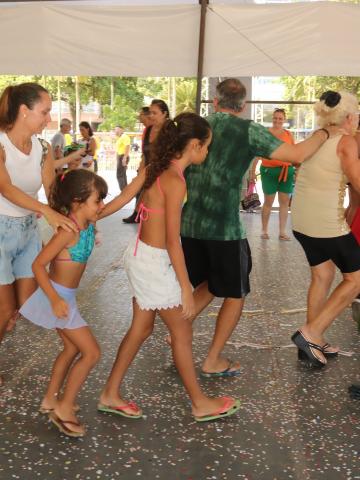 pessoas dançam sob tenda com confetes no chão. #paratodosverem
