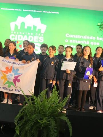 crianças seguram bandeira em palco #paratodosverem