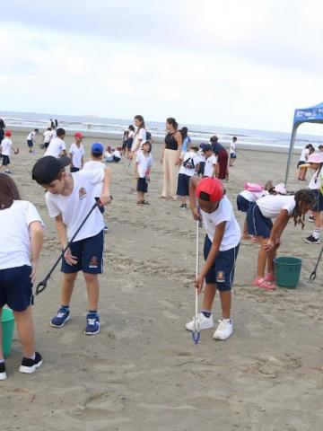 alunos uniformizados recolhem resíduos da areia da praia. #paratodosverem