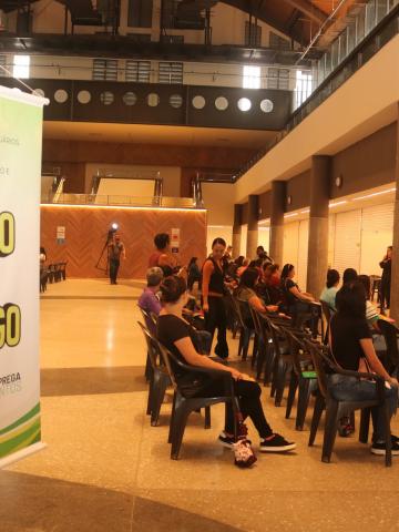 banner sobre mutirão com pessoas sentadas ao fundo. #paratodosverem