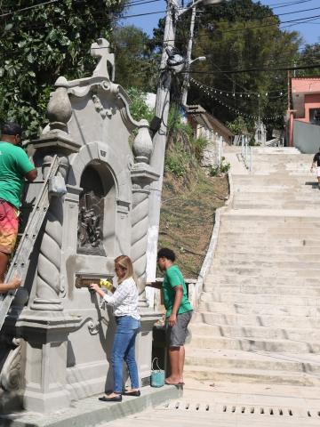 quatro pessoas em torno de um nicho junto à escadaria de morro. #paratodosverem