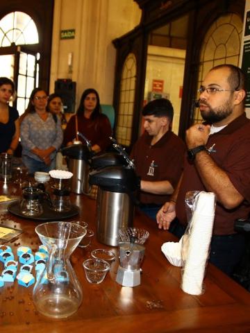 pessoa fala com mesa com café e doces para outras pessoas #paratodosverem