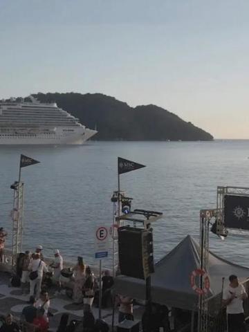 público na avenida de frente para o mar e navio ao fundo. #paratodosverem