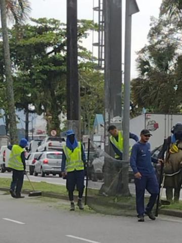 homens uniformizados trabalham na manutenção de canteiro em rua. #paratodosverem