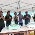 Quatro mulheres e dois homens batem palmas atrás de mesa com bolo de aniversário na cor verde