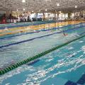 Vista geral da piscina olímpica com nadadores competindo e público ao fundo. #Pracegover