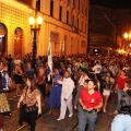 grande volume de pessoas caminha por rua do centro histórico à noite. Os postes de modelo republicano estão acesos. #paratodosverem 