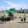 Ambulantes ao lado de um carrinho na praia #paratodosverem