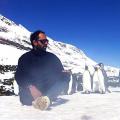 O velejador Amyr Klink sentado na neve com pinguins em volta. #pracegover