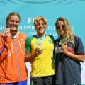 Ana Marcela e outras duas atletas exibem medalhas no pódio da prova. #pratodosverem