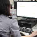 Mulher está de costas para a imagens, sentada e movimentando o mouse de um computador. A tela está aberta no portal da Prefeitura. #Pracegover