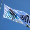 a bandeira no alto do mastro com a arte da santa e o distintivo do clube. #paratodosverem