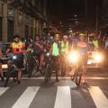 ciclistas param diante de faixa de pedestre para foto. É noite. Eles acenam. #paratodosverem