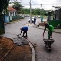 homens passam concreto em trecho de calçada. Um deles aplica a massa. O outro está segurando um carrinho de mão. #paratodosverem 