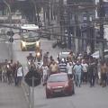 vários homens caminhando por rua atrás de um carro vermelho. #paratodosverem