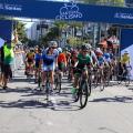 ciclistas estão iniciando a prova. Há um portal ao fundo onde se lê no alto Santista de ciclismo. #paratodosverem 