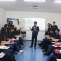 aprendizes estão sentados em sala. Alguns estão em pé. Um deles, o principal, no meio da sala, fala ao grupo. #paratodosverem