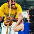 mestre toca berimbau diante de criança. #paratodosverem