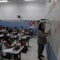 professora escreve no quadro e estudantes olham em sala de aula #paratodosverem