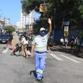 Agente de trânsito estende o braço. Atrás, pessoas atravessando a faixa de pedestre. #paratodosverem