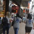 duas voluntárias estão caminhando na rua de costas para a foto. Elas usam camiseta de identificação do programa. #paratodosverem 