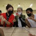 professora com vestuário japonês ensina dois alunos a segurarem hashi. #paratodosverem