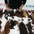 várias mechas de cabelo dispostas sobre uma mesa. Ao fundo aparecem as mãos de uma mulher. #paratodosverem 