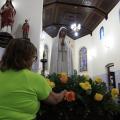 mulher arruma arranjo de flores na frente da santa #paratodosverem