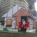 papai noel e mamães noel na frente da casinha na praça #paratodosverem
