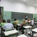 alunos adultos estão sentados em sala de aula. Professora está em pé falando ao grupo. #paratodosverem