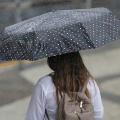 Mulher está de costas para a foto. Ela segura um guarda-chuva na rua. Está chovendo. #Paratodosverem