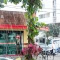 chuva caindo em rua. com estabelecimento comercial ao fundo e pessoas na rua. #paratodosverem