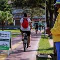 Agente de trânsito observa passagem de ciclista na ciclovia ao lado de placa com a inscrição Uma bike a mais Um carro a Menos. #pracegover