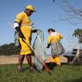 homem e mulher uniformizados removem folhas de jardim da orla. #paratodosverem