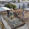 homens estão na parte superior de uma estrutura no alto de um prédio. Eles lançam e assentam concreto sobre armação de ferro. #paratodosverem