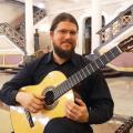 Bruno Henriques Hasper está sentado segurando um violão. #paratodosverem